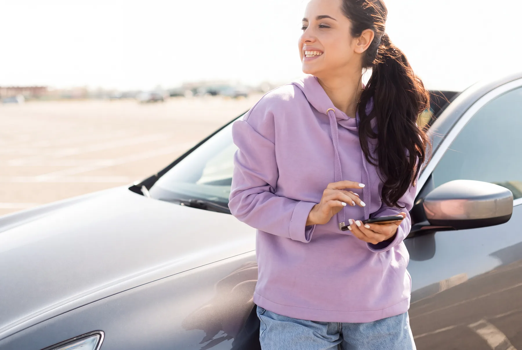 Mensalista encostada no carro, olhando o celular
